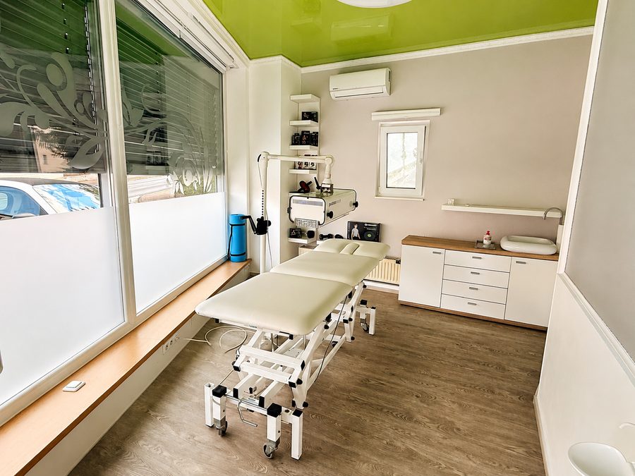 Behandlungsraum mit Liege am Fenster und grün gestalteter Decke